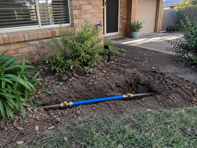 Exposed repaired water pipe in a yard trench beside a brick house in Whitebridge
